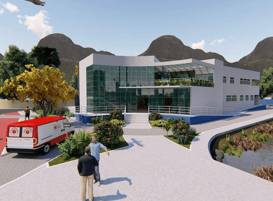 Maquete eletrônica do futuro Centro de Saúde da Enseada. O projeto apresenta um edifício moderno de dois pavimentos, com fachada branca e amplas paredes de vidro, cercado por jardins, paisagismo e rampas de acessibilidade.